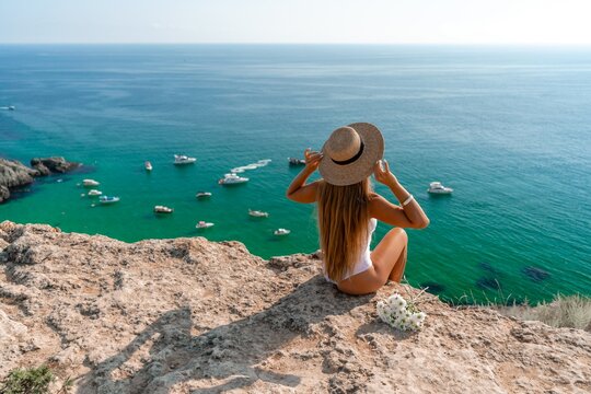 Woman travel sea. Happy woman in a beautiful location poses on a cliff high above the sea, with emerald waters and yachts in the background, while sharing her travel experiences