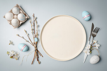 Happy Easter composition for easter design. Elegant Easter eggs, plate and flowers on pastel blue background. Flat lay, top view, copy space.