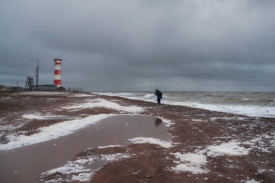Lighthouse on the shore. Difficult way to the lighthouse. A man in motion, seen from the back, is walking with difficulty along the shore of a stormy sea.