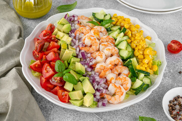 Shrimp salad with vegetables and olive oil mustard dressing. Fresh seafood salad on a white plate on a gray concrete background. Healthy food. Copy space.