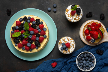 Homemade cake with fresh berries and sweet desserts on dark background.