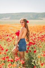 Naklejka na ściany i meble Woman poppies field. portrait happy woman with long hair in a poppy field and enjoying the beauty of nature in a warm summer day.