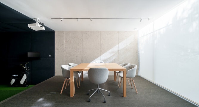 Modern meeting room with concrete walls, a wooden table, and grey upholstered chairs, complemented by soft lighting