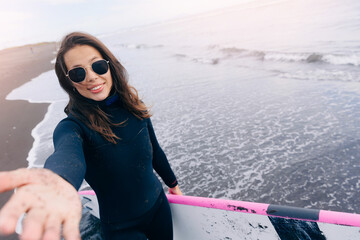 Extreme selfie photo of happy surfer woman in wetsuit with surfboard, winter surfing in ocean,...