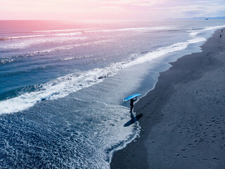 Surfer in wetsuit going to surf at black beach, Aerial top view. Lifestyle Extreme winter surfing...