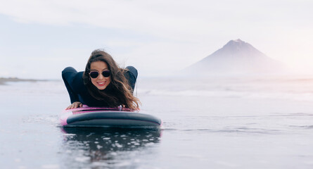 Extreme surfer woman in wetsuit with surfboard go to winter surfing in Atlantic ocean Kamchatka Russia. Adventure travel sport concept