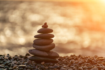 Balanced rock pyramid on pebbles beach. Golden sea bokeh on background. Selective focus, zen stones...