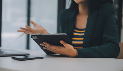 Charming Young asian businesswoman sitting on laptop computer in the office, making report calculating balance Internal Revenue Service checking document.