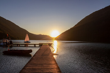 Wooden pier at the east shore of alpine lake Weissensee at sunset. Small sailinng boat with scenic...