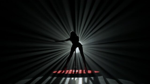 Portrait of young female dancer in the studio. Professional pole dancer girl silhouette dancing modern pole dance against bright spotlight.