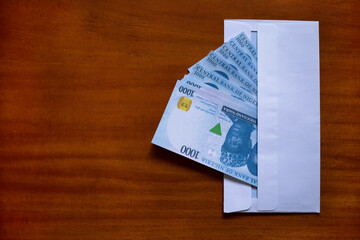 1000 Nigerian Naira notes showing from a white envelope on polished brown wooden background with copy space.