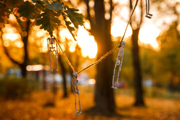 A garland of skeletons hung on trees in an autumn park at sunset, the concept of Halloween, copy...