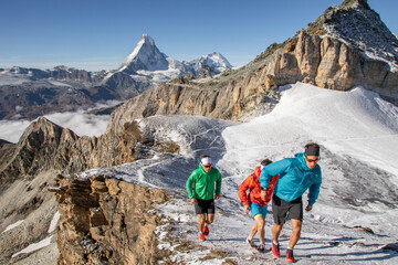 Three trail runners in colorful attire running on a snowy mountain