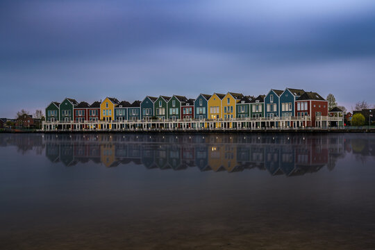 Colorful row houses with reflections on the calm waters of Houten's Rietplas at dusk