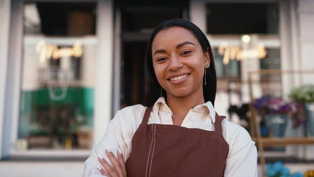 Cute african waitress in apron looking at camera and welcoming guests at door of cafe 