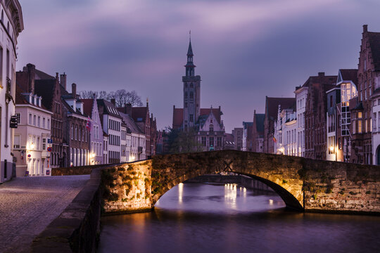 Twilight settles over the tranquil canals and medieval buildings of Brugge, Belgium, with a stone bridge in the foreground