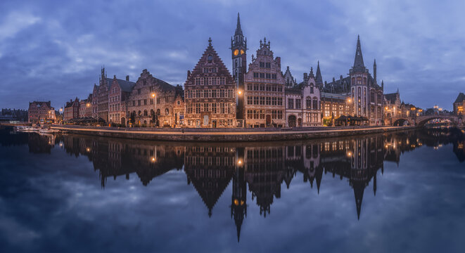 The historic buildings of Ghent are mirrored in the calm waters during twilight, showcasing the city's medieval charm