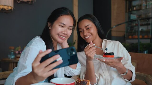 Funny multicultural female friends taking cell phone selfies with cake at cafe