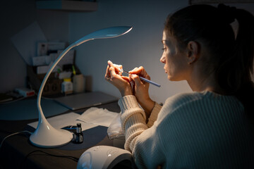 Attractive woman doing herself a manicure at home in the evening in a dark room