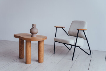 Minimalist interior featuring a wooden coffee table with a ceramic vase and a modern chair on a white floor.