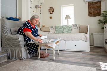 An elderly woman collecting puzzle while sitting in a chair in her bright room at home.