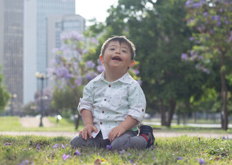 White boy with down syndrome sitting on the grass playing in a park