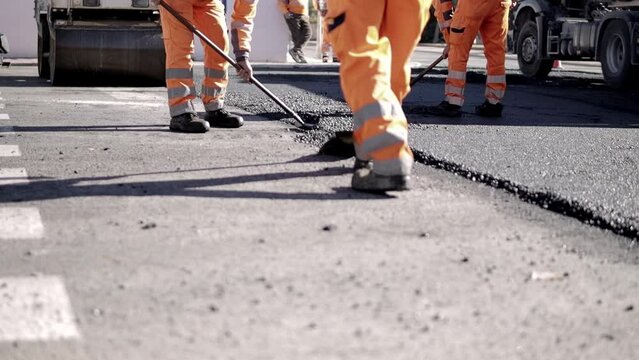 A team of workers lays hot asphalt on the street along the road. steamroller. Road builders