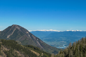 Scenic view on Sinacher Gupf in Karawanks mountains and the Drava river in Rosental valley in Carinthia, Austria. Forest in early spring. Snow capped Hohe Tauern mountain range can be seen. Sunny day