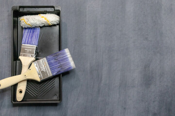Paint brushes, roller in black tray on gray painted background with copy space