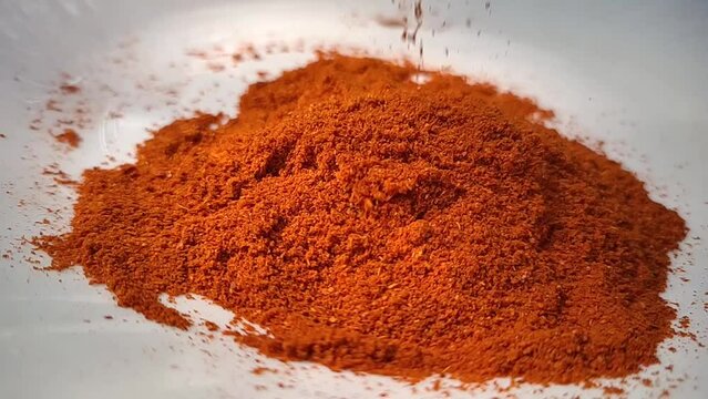 Organic spicy red hot chilli pepper powder or dust falling on a pile of cayenne pepper powder isolated and scattered on a white background surface. Closeup macro slow motion view.