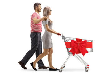 Profile shot of a young couple walking and pushing a shopping cart tied with a red ribbon bow