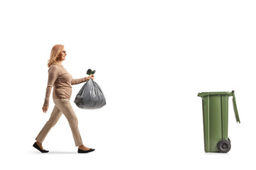Full length profile shot of a middle aged woman carrying a plastic waste bag and walking towards a...