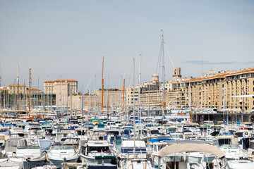 Motor and sailboats are tightly parked in the marina of Marseille against the backdrop of the city.