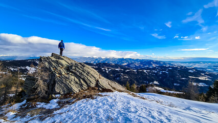 Naklejka na ściany i meble Man with backpack standing on massive rock formation at Steinerne Hochzeit, Saualpe, Lavanttal Alps, border Styria Carinthia, Austria, Europe. Panorama of alpine meadows and snowcapped mountains