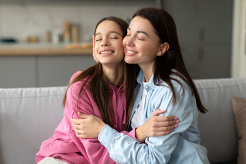 Happy mother and teenage daughter hugging cuddling, spending time together at home, smiling with...