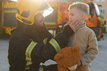 A firefighter take a little child boy to save him. Fire engine car on background