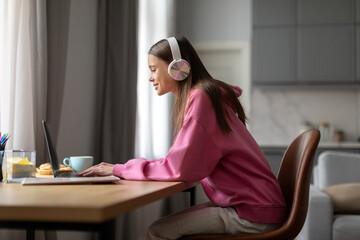 Distant learning concept. Happy smiling teenage student girl in headphones with laptop computer at...