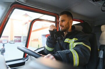 Firefighter using radio set while driving fire truck - obrazy, fototapety, plakaty