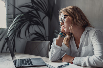 Discontented thoughtful woman with hand under chin bored at work, looking away sitting near laptop, demotivated office worker feels lack of inspiration, no motivation, boring routine, creative crisis.