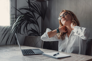 Exhausted young Caucasian female worker sit at desk massage neck suffer from strain spasm muscles....