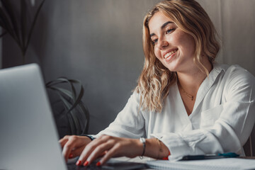 Happy young blonde business woman entrepreneur using computer looking at screen working in internet sit at office desk, smiling millennial female professional employee typing email on laptop at work - obrazy, fototapety, plakaty