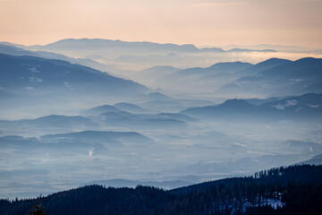 Panoramic view of magical blue mountain range of Lavanttal Alps, Carinthia, Austria. Valley is covered by mystical fog. Winter wonderland in Wolfsberg, Austrian Alps. Ski touring on Saualpe. Freedom