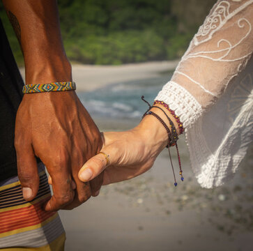 Close-up of loving couple holding hands in Costa Rica. Surfer man with bracelet and woman with beautifully hands on beach on summer day. Love, vacation, family concept