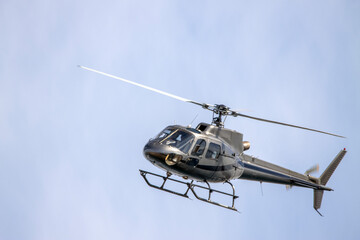 A gray helicopter crosses the blue sky with clouds. Transportation. Urban.