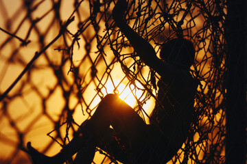 Silhouette of a person climbing a fence against a beautiful sunset backdrop. Ideal for illustrating determination, overcoming obstacles, or breaking free from constraints