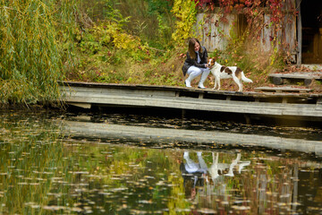 Young beautiful girl petting a dog near a lake in an autumn park
