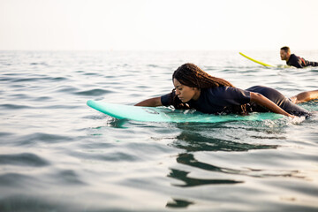 An African couple is surfing in the sea. The young people are swimming on the surfboard breaststroke style. The black woman with long hair is in the foreground. Copyspace for surf advertising.