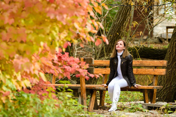 A young beautiful girl sits on a bench and enjoys the autumn landscape