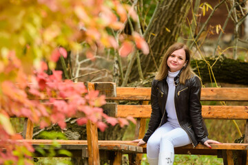 A young beautiful girl sits on a bench in an autumn park