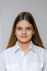 Portrait of a fourteen-year-old girl in a white shirt on a gray background